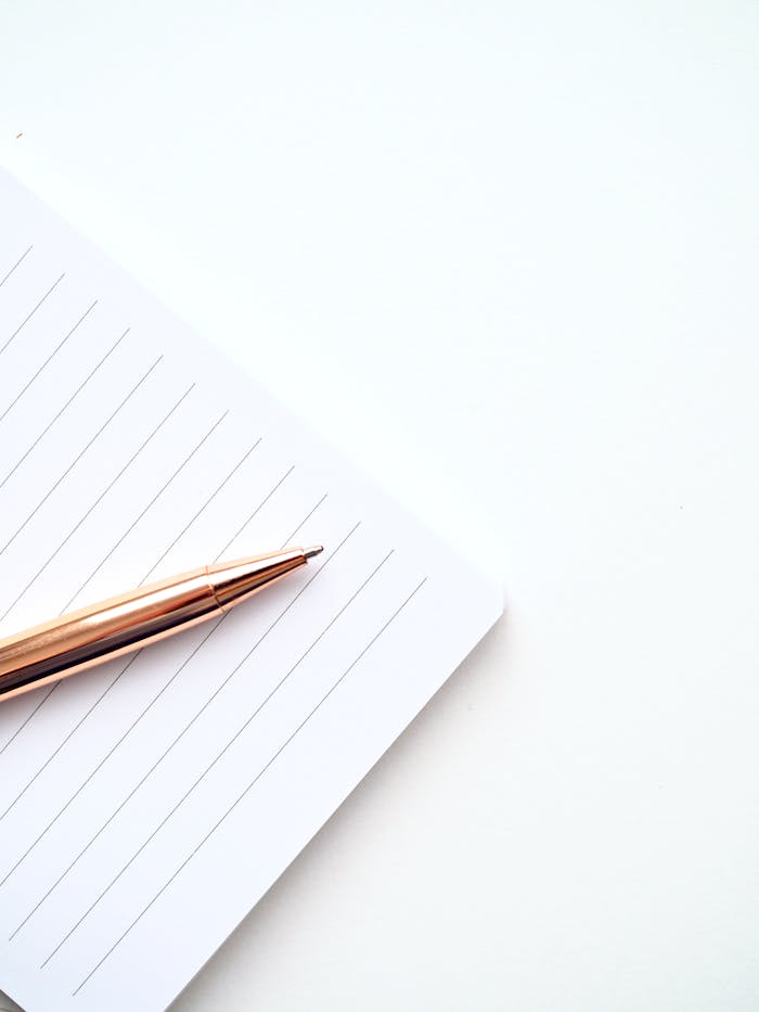 A close-up shot of a gold pen on a lined notepad with a white background, offering ample copyspace.