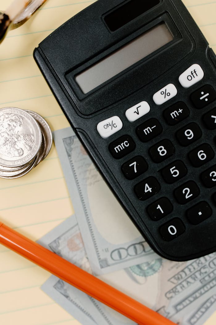 services-04 Black calculator, coins, and cash on a yellow notepad with a pencil.